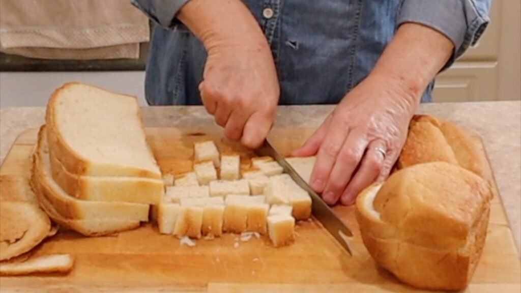 woman cutting fresh sliced bread into cubes on a cutting board