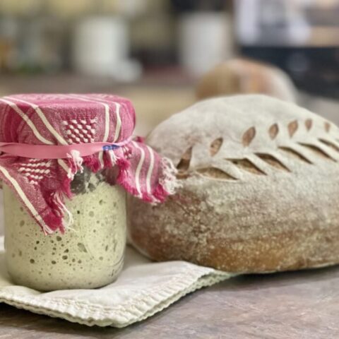 sourdough starter sitting beside a fresh baked loaf of sourdough bread