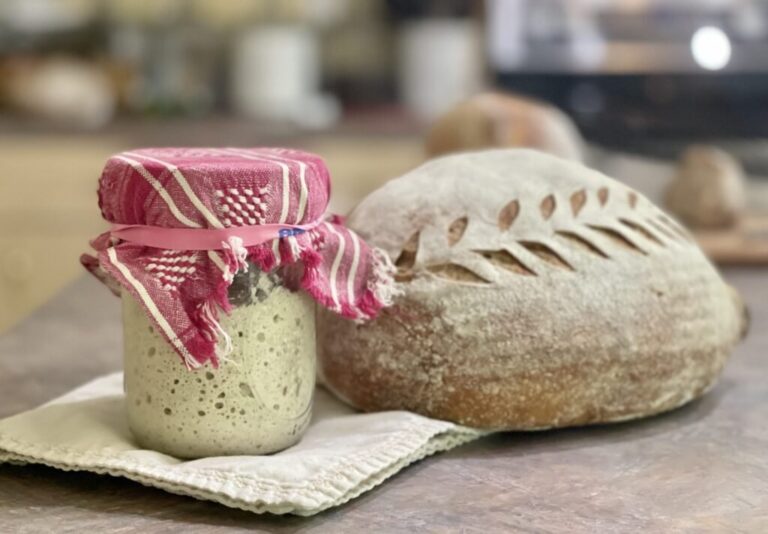 sourdough starter sitting beside a fresh baked loaf of sourdough bread