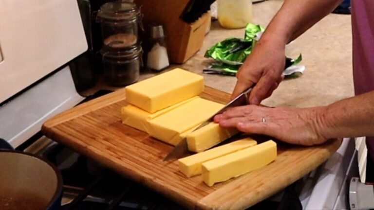 slicing sticks of butter on a cutting board in preparation to make ghee or clarified butter