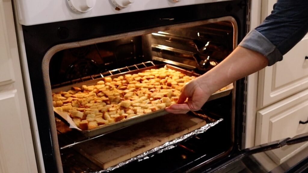 woman placing a large tray of cubed bread in the oven for roasting to make croutons