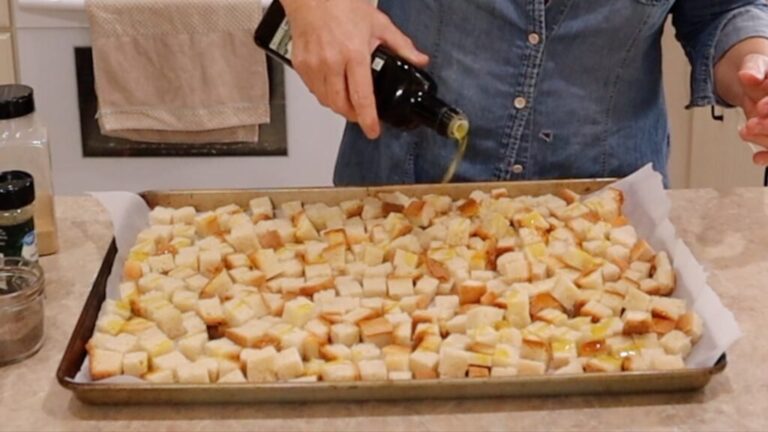 drizzling olive oil over cubed bread layered on a baking sheet