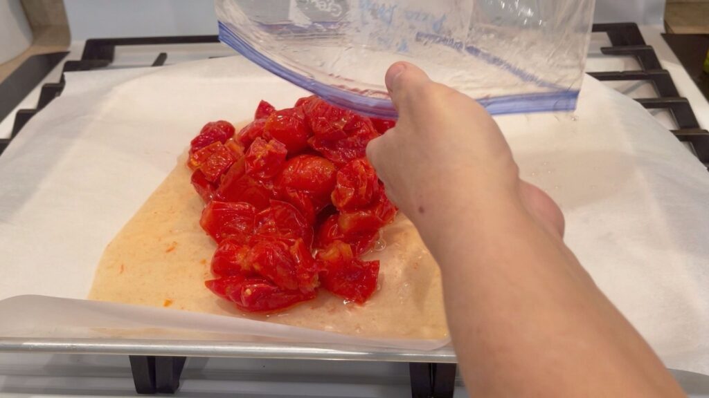 previously frozen, cored tomatoes being poured out of a freezer bag and onto a baking sheet lined with parchment paper