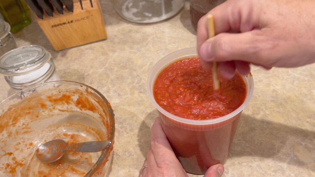 stirring out the air bubbles in the marinara that has been place into a 16 oz. deli container for storage