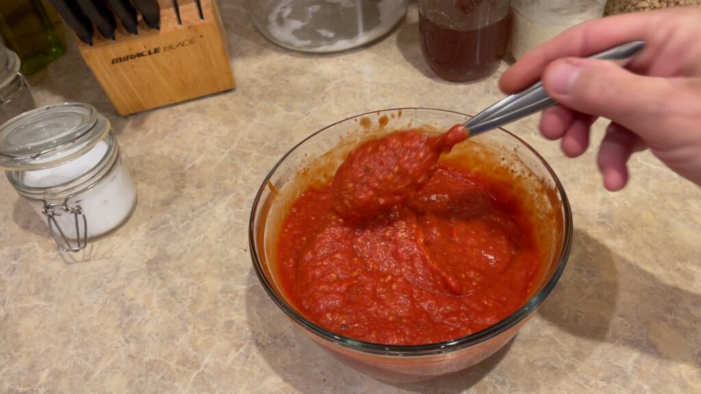 spoonful of roasted tomato marinara held above a bowl of marinara showing the thick, smooth texture of the sauce.