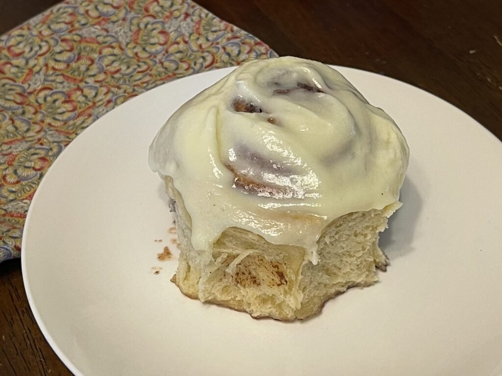 freshly baked and iced sourdough cinnamon roll on a white plat