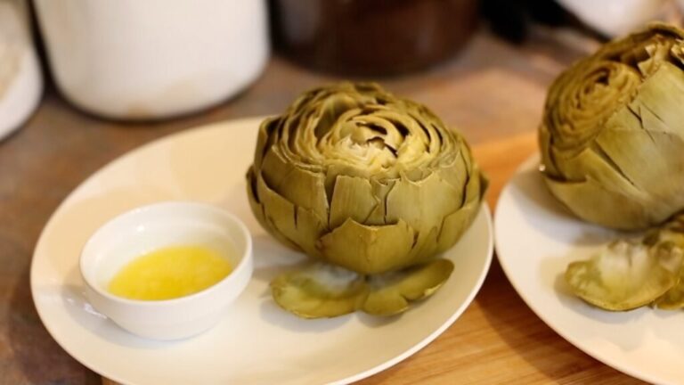 perfectly cooked artichoke sitting on a white plate next to a small bowl of melted butter