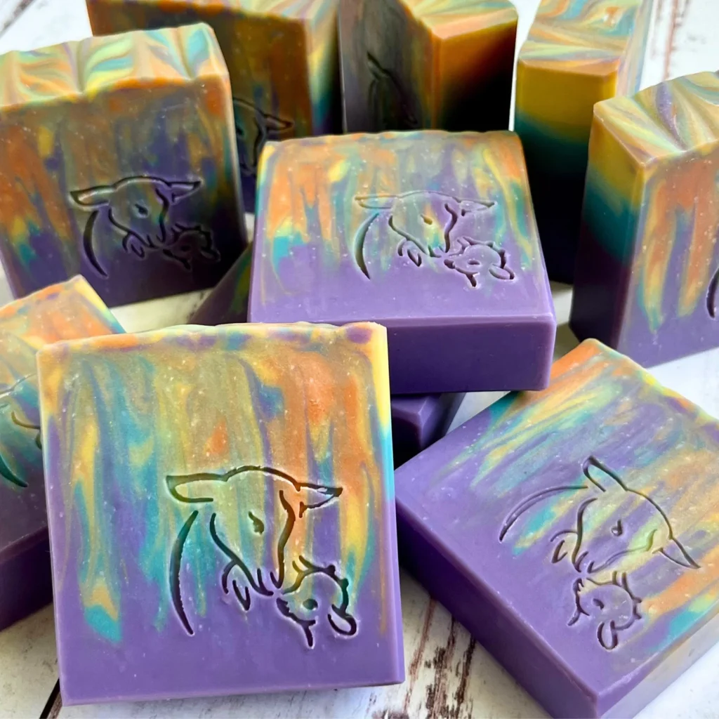 goat milk soap designed with a purple base and blue, green, yellow, and orange pushed from top to over halfway down.