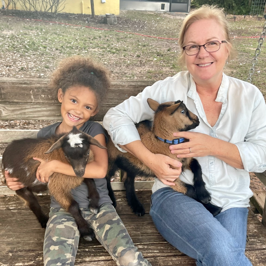 young girl and woman both holding a baby goat and sitting on a swing outside